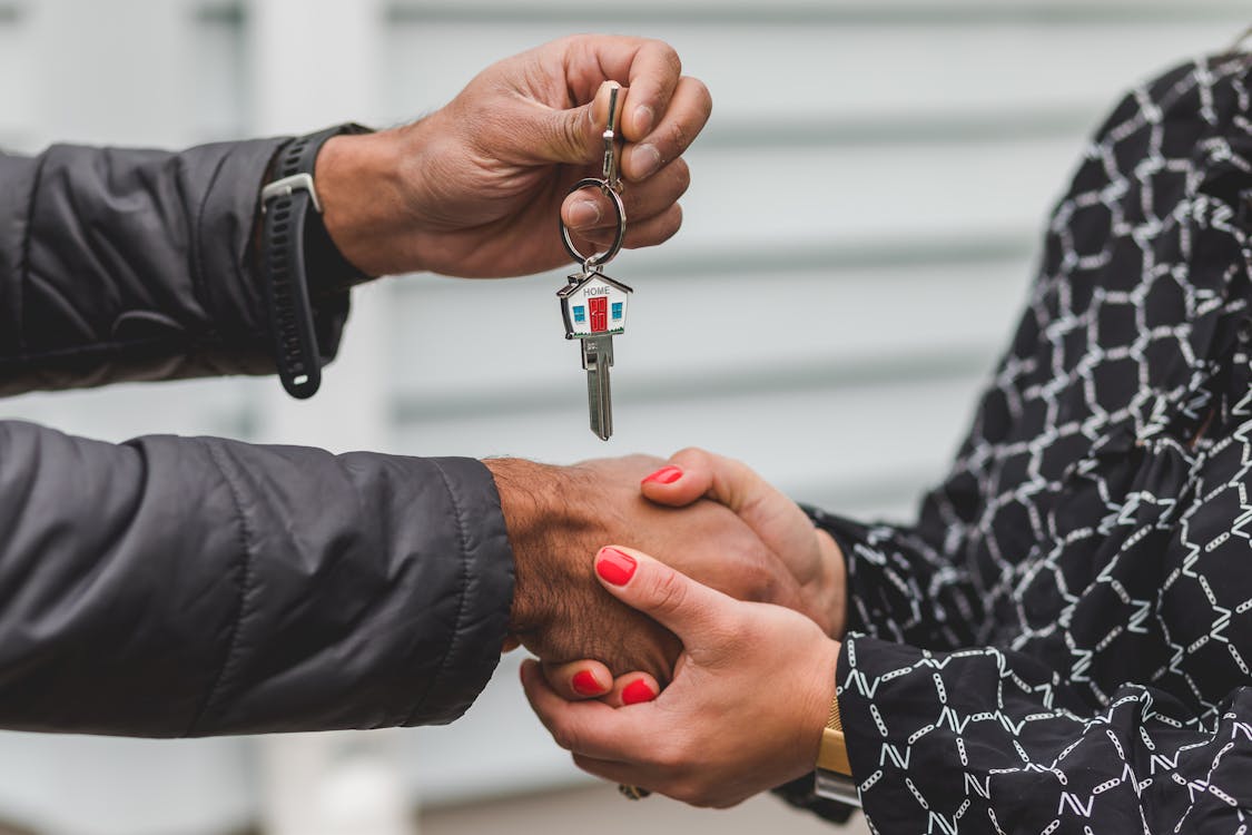 A close-up, professional shot of one hand passing a set of modern house keys to another, symbolizing a successful and smooth real estate transaction.