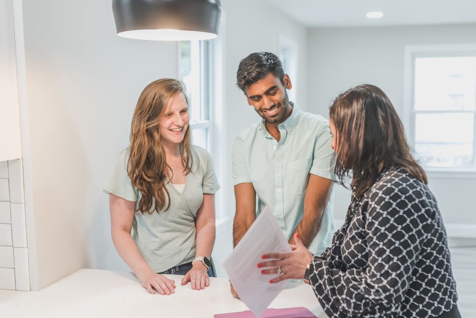 A smiling couple sits at a table in a bright, modern home, signing documents, which conveys the financial relief and happiness of saving money on commissions.
